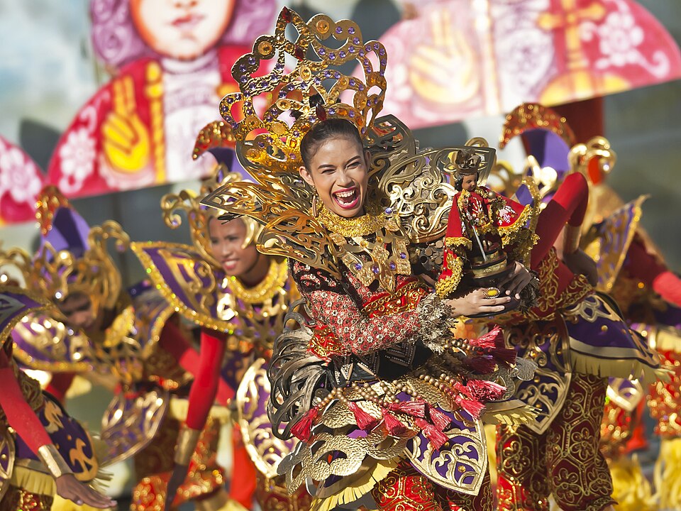 シヌログ祭りで華やかな金色と赤の衣装をまとって踊る人々